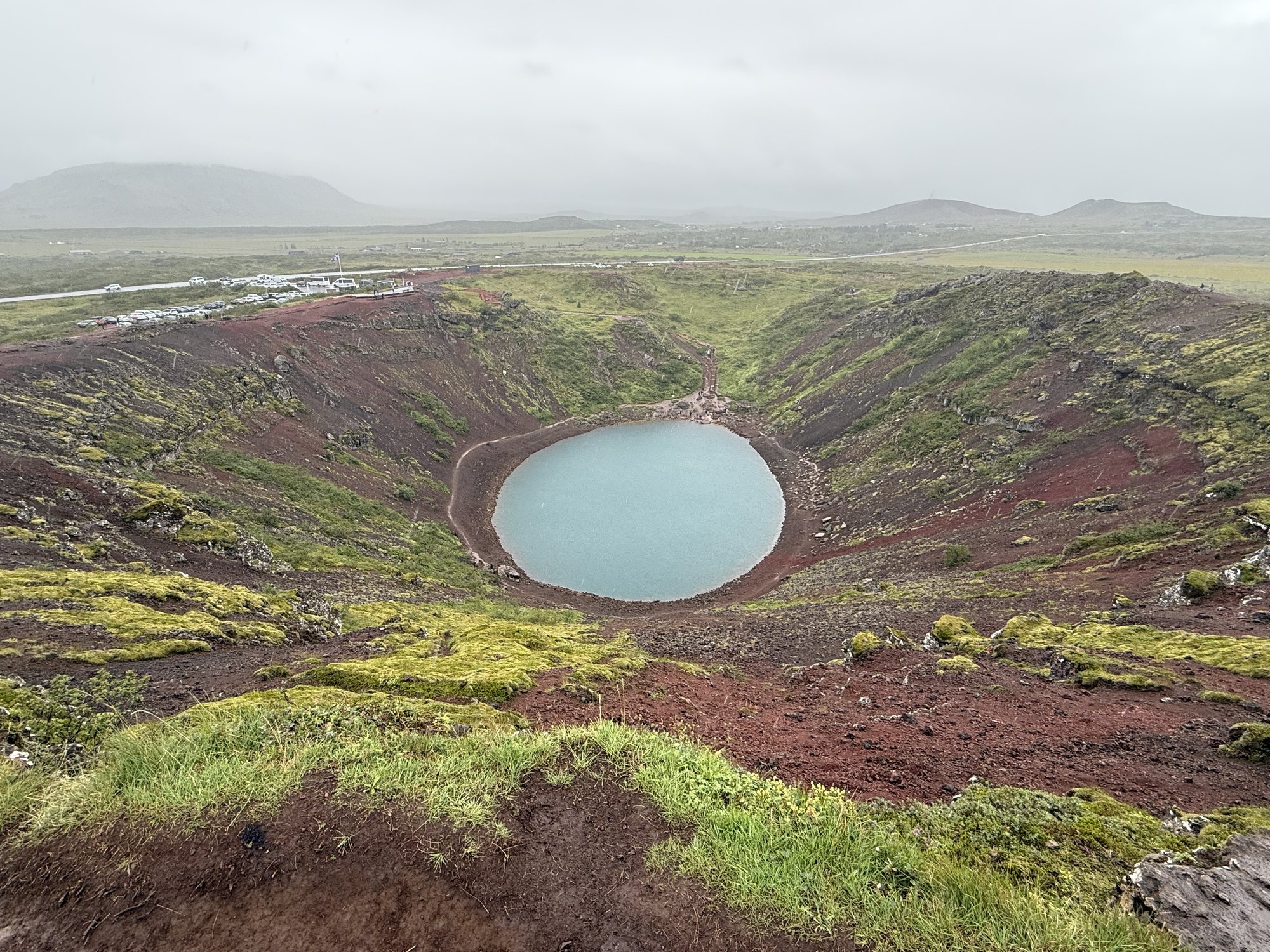 Kerið Volcanic Crater, red slopes meeting aqua water